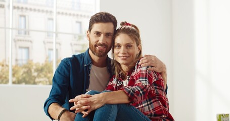 Caucasian joyful young couple wife and husband sitting in room hugging together, embracing, looking at camera and smiling. Family time. Repair and improvement. renovate home. Close up concept