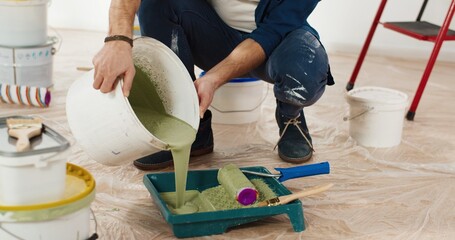 Close up of Caucasian young handsome man pouring green olive paint preparing for painting walls in...