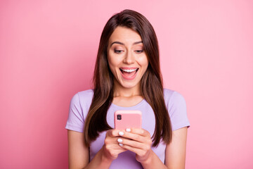 Photo portrait of excited woman holding phone in two hands with open mouth isolated on pastel pink colored background
