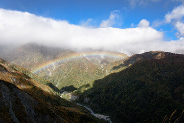 It is a mountain range of Hakuba in Nagano prefecture, Japan. There is a rainbow in the valley of the mountains. It is a very beautiful photo under the blue sky.