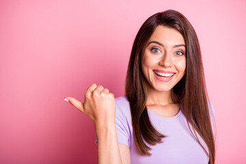 Photo portrait of pretty girl smiling showing with finger on blank space recommending isolated on pastel pink color background