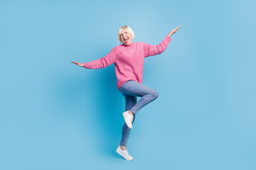 Photo portrait full body view of happy old lady dancing standing on one leg isolated on pastel blue colored background