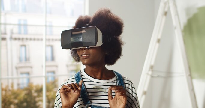 Close up of African American young woman stands in house wearing VR glasses and swiping scrolling with hands in air using modern innovations repairing and improving home. Virtual reality technology