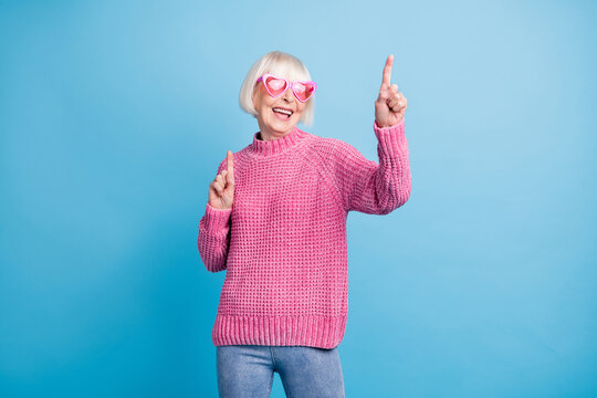 Photo Portrait Of Cute Elderly Lady Pointing Fingers Up Dancing Wearing Pink Glasses Isolated On Pastel Blue Colored Background