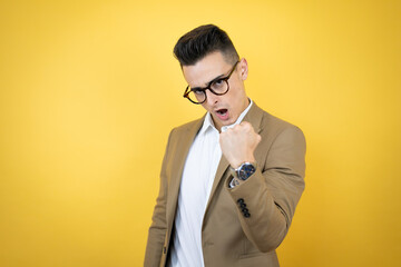 Young business man over isolated yellow background angry and mad raising fist frustrated and furious while shouting with anger. Rage and aggressive concept.