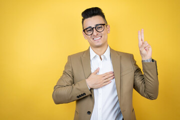 Young business man over isolated yellow background smiling swearing with hand on chest and fingers...