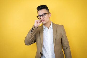 Young business man over isolated yellow background mouth and lips shut as zip with fingers. Secret...
