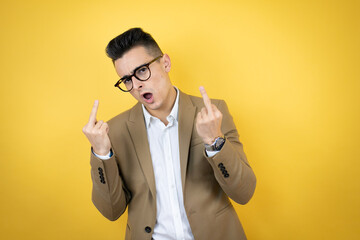 Young business man over isolated yellow background showing middle finger doing fuck you bad...
