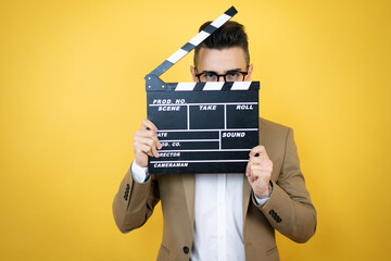 Young business man over isolated yellow background holding clapperboard very happy having fun