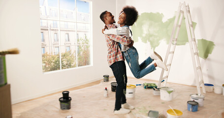 African American happy young cute couple hugging and embracing in new apartment during home repair...