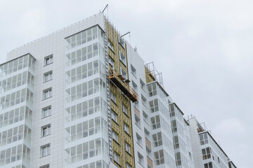 Construction of a multi-storey building. Empty hanging cradle. Wall insulation and mounting of a...