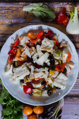 cod boiled with winter cherry tomatoes, black olives, celery, onion, pickled peppers on wooden background. Selective focus.