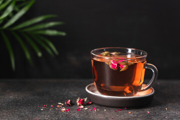 Fresh tea from rose petals in glass cup. Pink hot drink on dark brown background