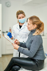 Obraz premium Mass vaccination of the population. Female doctor in a mask gives the patient documents to sign before giving her the Covid-19 antiviral vaccine