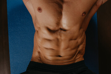 A photo from above of the abs of a bodybuilder during doing crunches on a blue yoga mat.