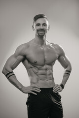 Fototapeta na wymiar A black and white photo of a muscular man with a beard who is posing. The athletic guy is demonstrating his sporty physique. A bodybuilder with tattoos on his forearms is relaxing after hard training.