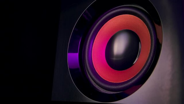 Audio speakers lit by colorful neon club lights. Professional studio subwoofer speaker isolated. Concept for dance music party. Close up. Slow motion.