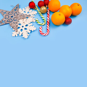 Christmas snowflakes, star, striped candy cane and tangerines on blue table. Free place for product or text. Christmas or new year frame / border. Square photo.