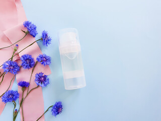 Mockup of transparent bottle of intimate lubricant gel,  blue wild flowers and pink silk ribbon on pastel blue background. Bottle for branding and label. Natural organic cosmetics