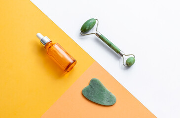 Face serum, gua sha and jade roller on geometric background. Anti aging skin care product