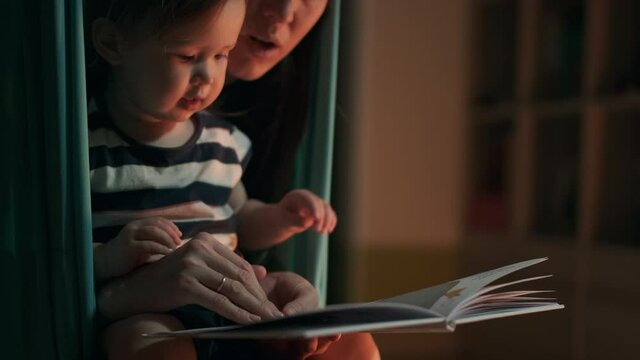 Baby and mother read a hammock. Mother reads a book with together girl being in the hammock at home
