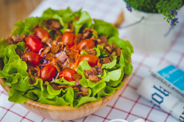 Bacon salad with vegetables and tomatoes serving in bow on the table with newspaper beside