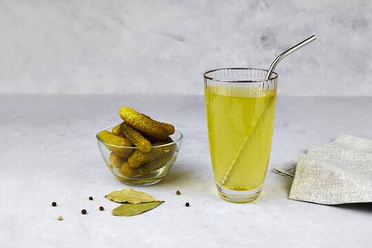Cucumber Pickle Or Pickle Juice In Glass With A Metal Tube For Drinks , A Bowl With Pickled Gherkins On Light Background.  Trend Drink, Sports Nutrition, Healthy Supplements. Zero Waste