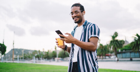 Smiling ethnic hipster messaging on smartphone in park