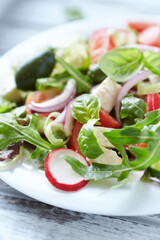 Salad with feta cheese, radish, rocket, green olives, tomatoes, cucumber and fresh basil. Bright wooden background. Close up. 