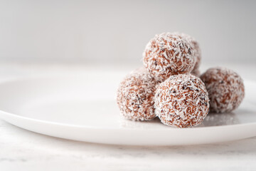 Candy balls made of dates and coconut shavings in a white dish on a light background near the copy space