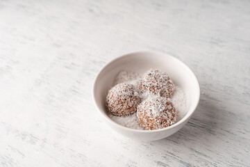 Round vegetarian sweets made from dates and coconut shavings in a white bowl with coconut shavings near the copy space