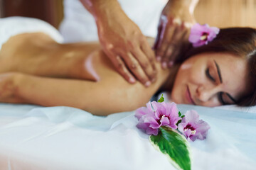 Purple flower lying down. Man does massage to the young woman in white towel indoors