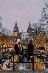 couple on city trip Amsterdam Netherlands canals with Christmas lights during December, canal...