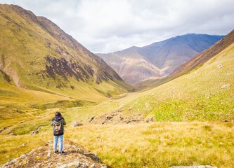 Backpacker woman stands on the rock overlooking scenic Juta valley in caucasus mountains. Kazbegi travel. Georgia