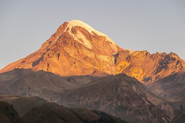 Beaitiful scenic view of KAzbek mountain top during sunrise and Gergeti church in foreground