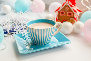 Obraz na płótnie Canvas A cup with a saucer with a drink against the background of tinsel and a gingerbread house