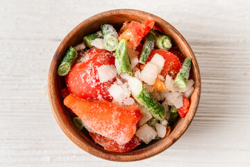 Frozen vegetables in bowl on light background