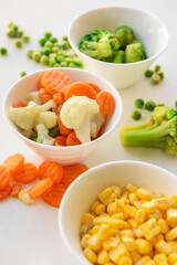 Frozen vegetables in bowls on white background