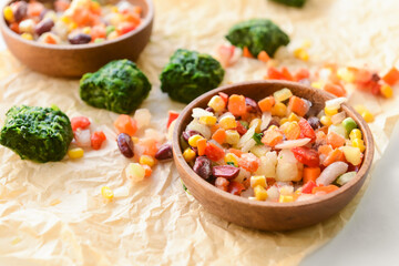 Frozen vegetables in bowl on light background