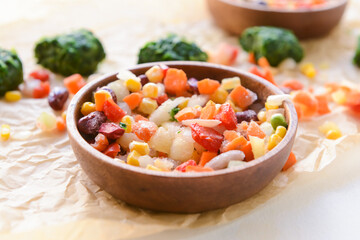 Frozen vegetables in bowl on light background