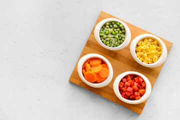 Frozen vegetables in bowls on light background