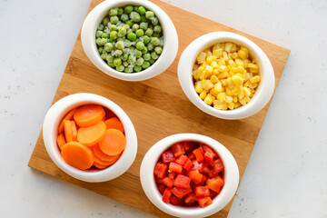 Frozen vegetables in bowls on light background