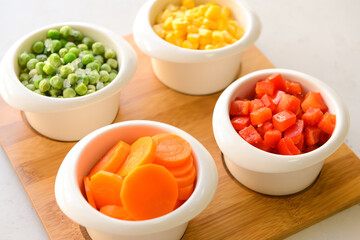 Frozen vegetables in bowls on light background