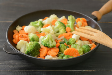 Frozen vegetables in bowl on wooden background