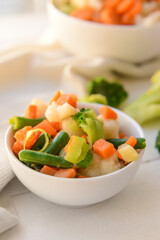 Frozen vegetables in bowls on light wooden background
