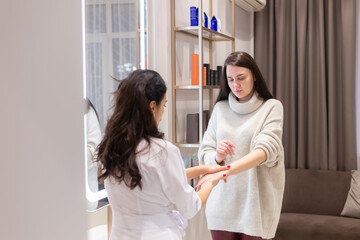 Fototapeta premium Two women, a beautician doctor and a client, stand at the mirror, for a consultation, the doctor applies cream to the woman's hands and makes a light massage