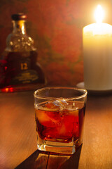 a glass of whiskey with ice is on the table, a candle is burning nearby