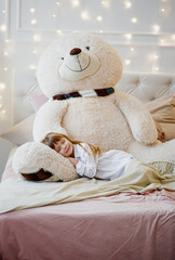 Sleeping girl at home at Christmas time with large Teddy bear plush toy.
