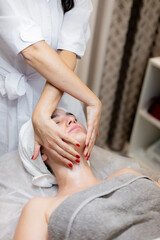 A young beautiful girl lies on the beautician's table and receives procedures, a light facial massage using oil. Woman takes care of herself, enjoys massage