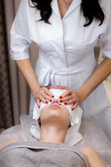 A young beautiful girl lies on the beautician's table and receives procedures, a light facial massage. Woman takes care of herself, enjoys massage